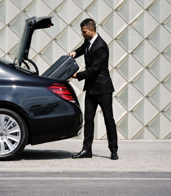 Chauffeur loading suitcase into luxury sedan
