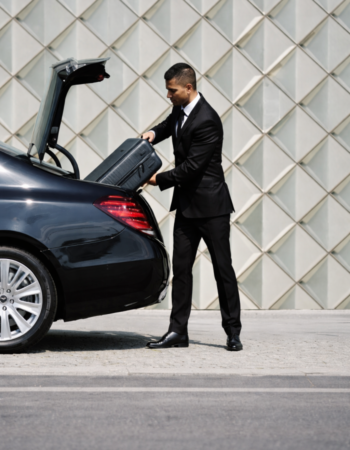Chauffeur loading suitcase into luxury sedan